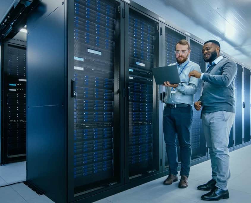 two IT workers look at laptop in data center