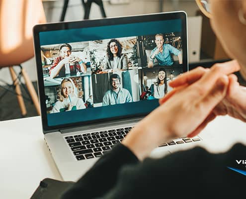 woman uses laptop to video conference with six coworkers