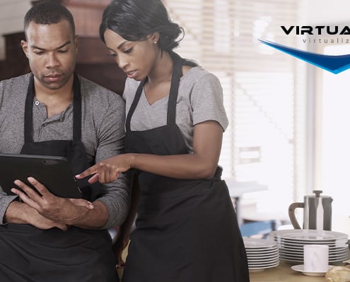 man in apron looks at tablet while woman in apron points at screen in commercial kitchen