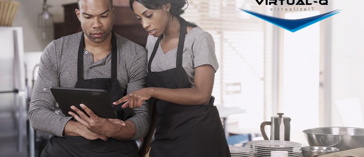 man in apron looks at tablet while woman in apron points at screen in commercial kitchen