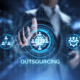 circular IT graphics above the word "outsourcing" over dark background with man in suit