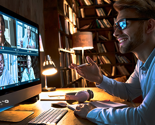 smiling man uses desktop computer to video conference with four coworkers