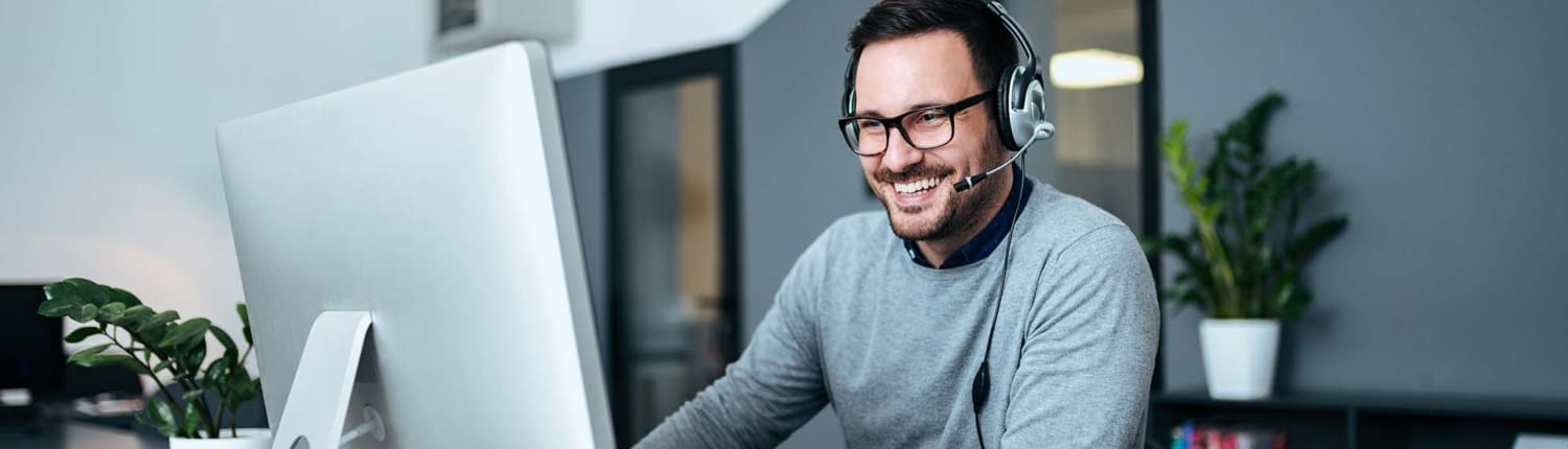 Smiling casual business man with headset working on the computer