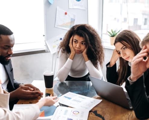 Image of exhausted team members meeting around a table.