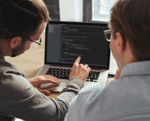 Image of two people looking at code on a computer.